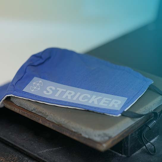 Blaue Maske mit STRICKER Logo liegt auf einem Tisch und wird gleich bedruckt.
