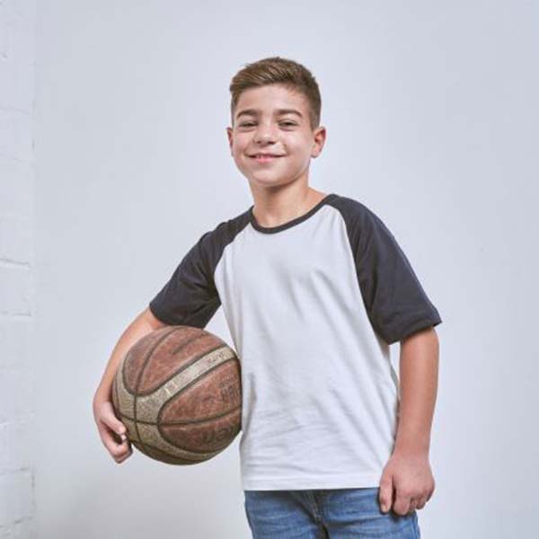 Blick auf einen Jungen, welcher ein weiß-grünes T-shirt trägt und einen Basketball in der Hand hält.