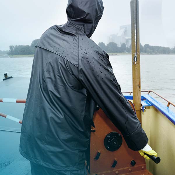 Blick auf einen Bootsführer, welcher wetterfeste Kleidung trägt.