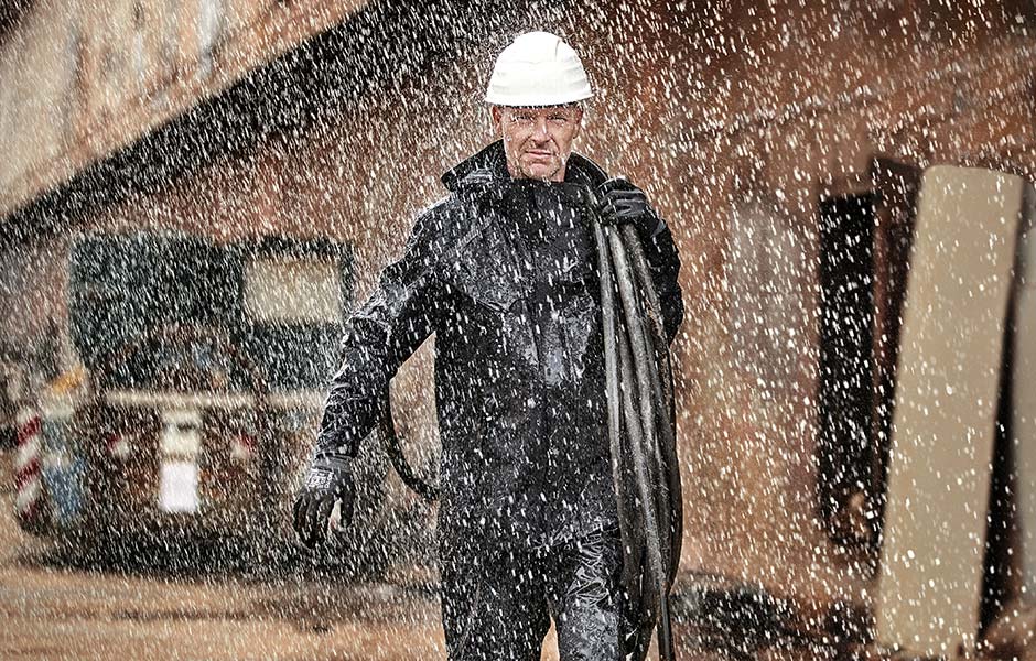 Blick auf einen Handwerker, welcher im Regen steht und wetterfeste Arbeitskleidung trägt.