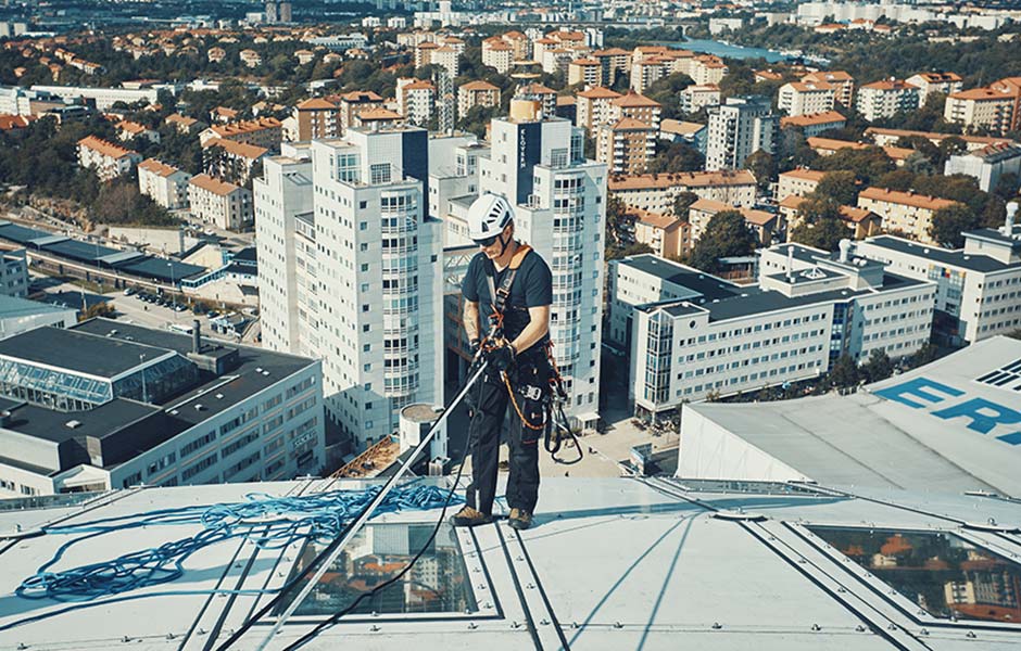 Blick auf einen Mann, welche ein Gebäude hoch klettert und dabei von einer Absturzsicherung gehalten wird. Im Hintergrund kann man eine Stadt sehen.