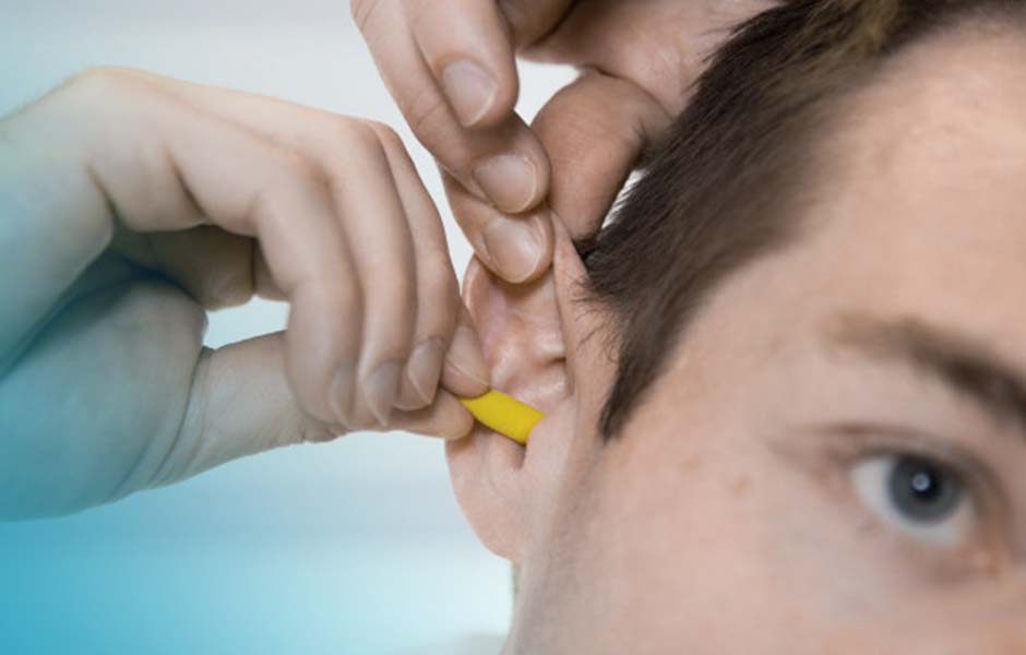 Ein Mann steckt sich gerade einen Gehörschutzstöpsel in die Ohren.