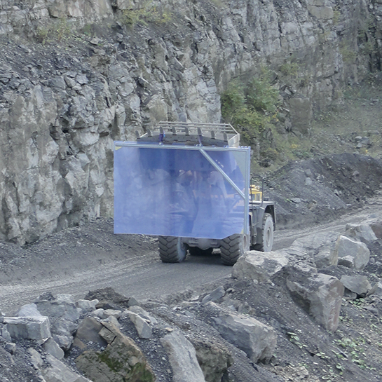 Eine riesige STRICKER Industrie-Pendeltür wird mit großem Gerät in einen Steinbruch transportiert und dort anschließend eingebaut.