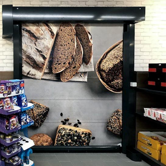 Blick aus einem Verkaufsraum auf ein STRICKER Schnelllauftor. Auf dem Motivbehang sind verschiedene Brote, Brotscheiben und Brötchen zu sehen.