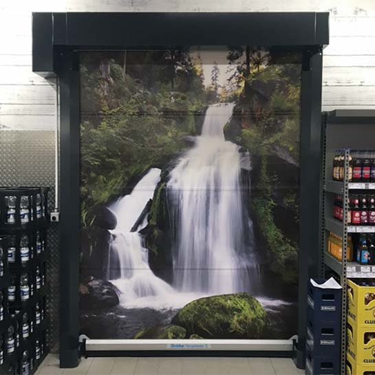 Blick auf ein STRICKER-Schnelllauftor, welches in einem Supermarkt eingebaut ist und ein Wasserfall als Motivbehang zeigt.