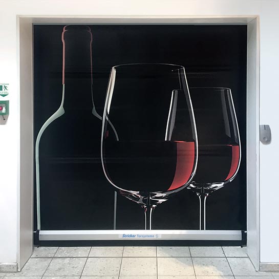 Auf einem STRICKER Schnelllauftor ist der Motivbehang mit einem dunklen Hintergrund und zwei gefüllten Rotweingläsern sowie einer Weinflasche im Vordergrund bedruckt.
